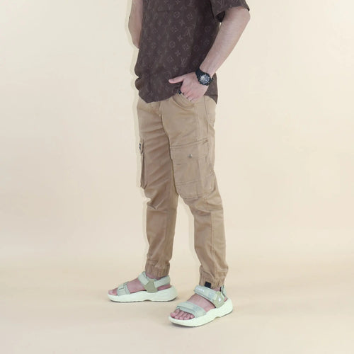 Person wearing brown cargo pants and sandals on a beige background