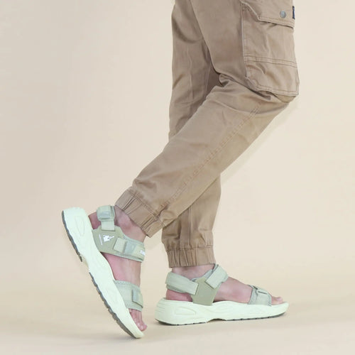 Person wearing light gray sandals and beige pants on a beige background