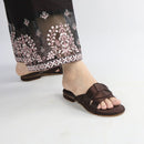 Brown sandal worn with black pants featuring white embroidery on a light gray background