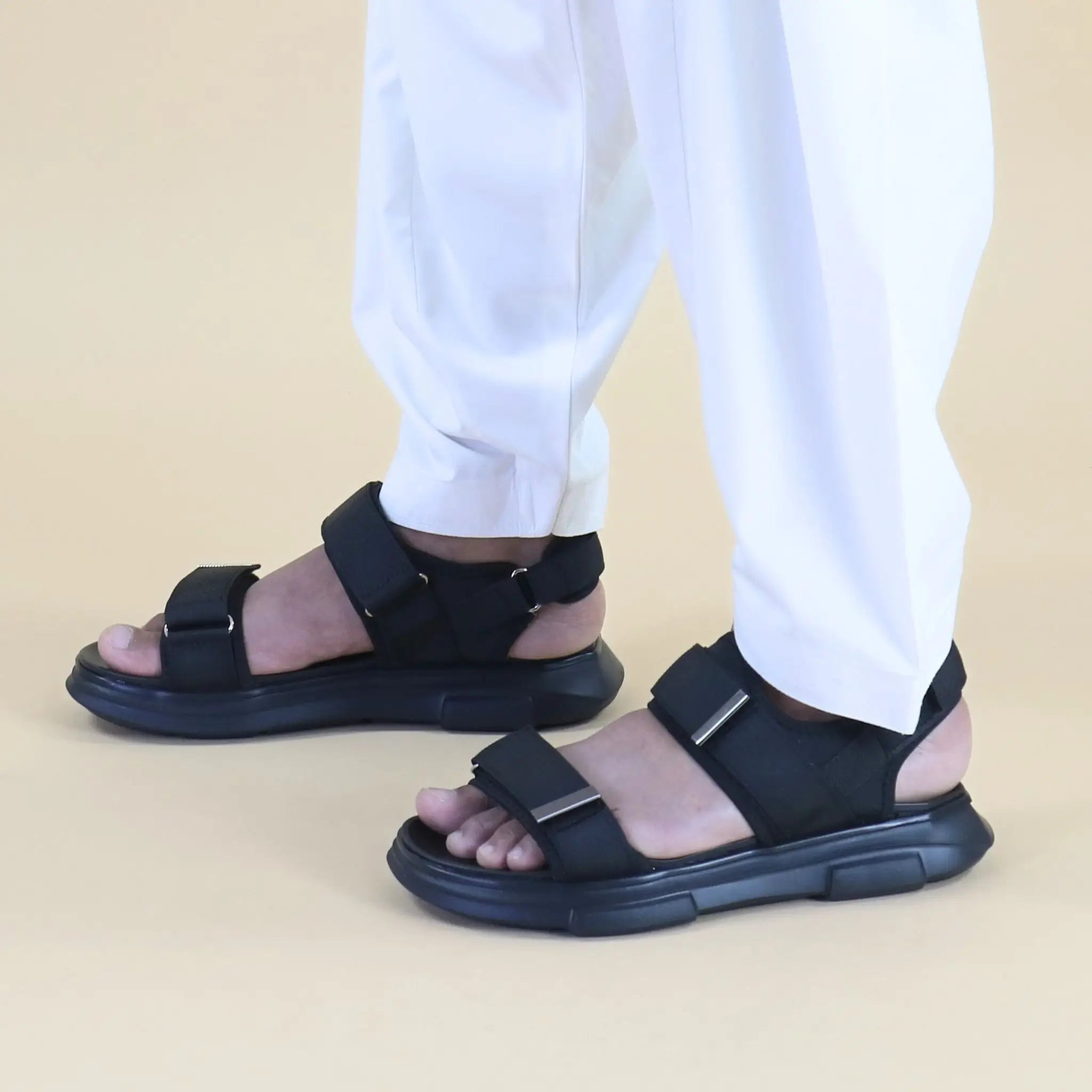 Black sandals worn with white pants on a beige background