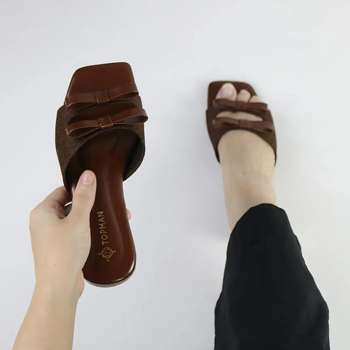 Brown sandals with a bow design held by a hand on a white background-topmanshoes